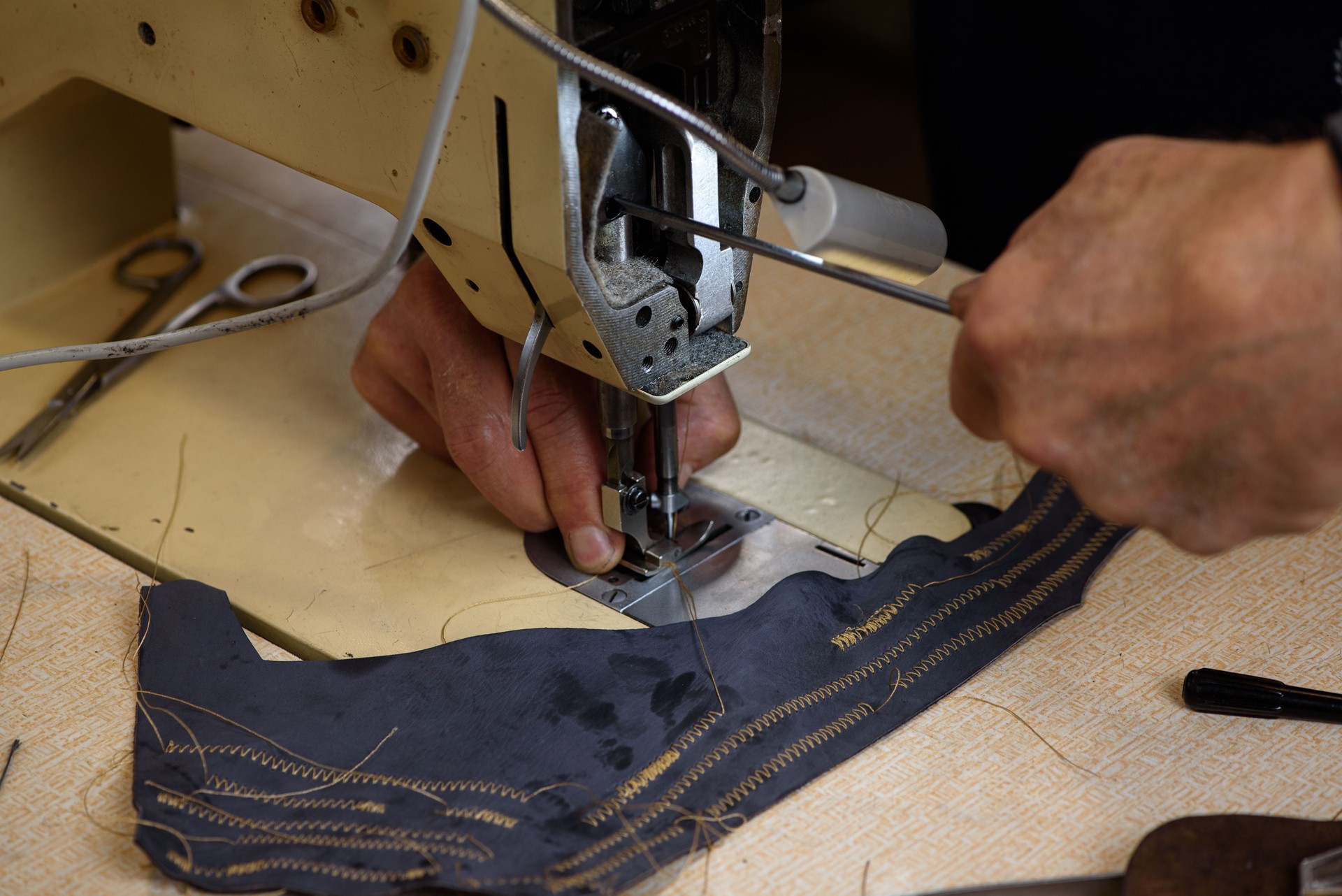 Mechanic repairing industrial sewing machine in factory. Hands of repairman fixing problems and testing professional overlock in shoemaker workshop. Closeup.